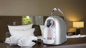 Eine Kaffeemaschine auf einem Tisch mit zwei weißen Tassen und Untertassen, einer kleinen Schale und einer Kaffeekapsel-Auswahl.
