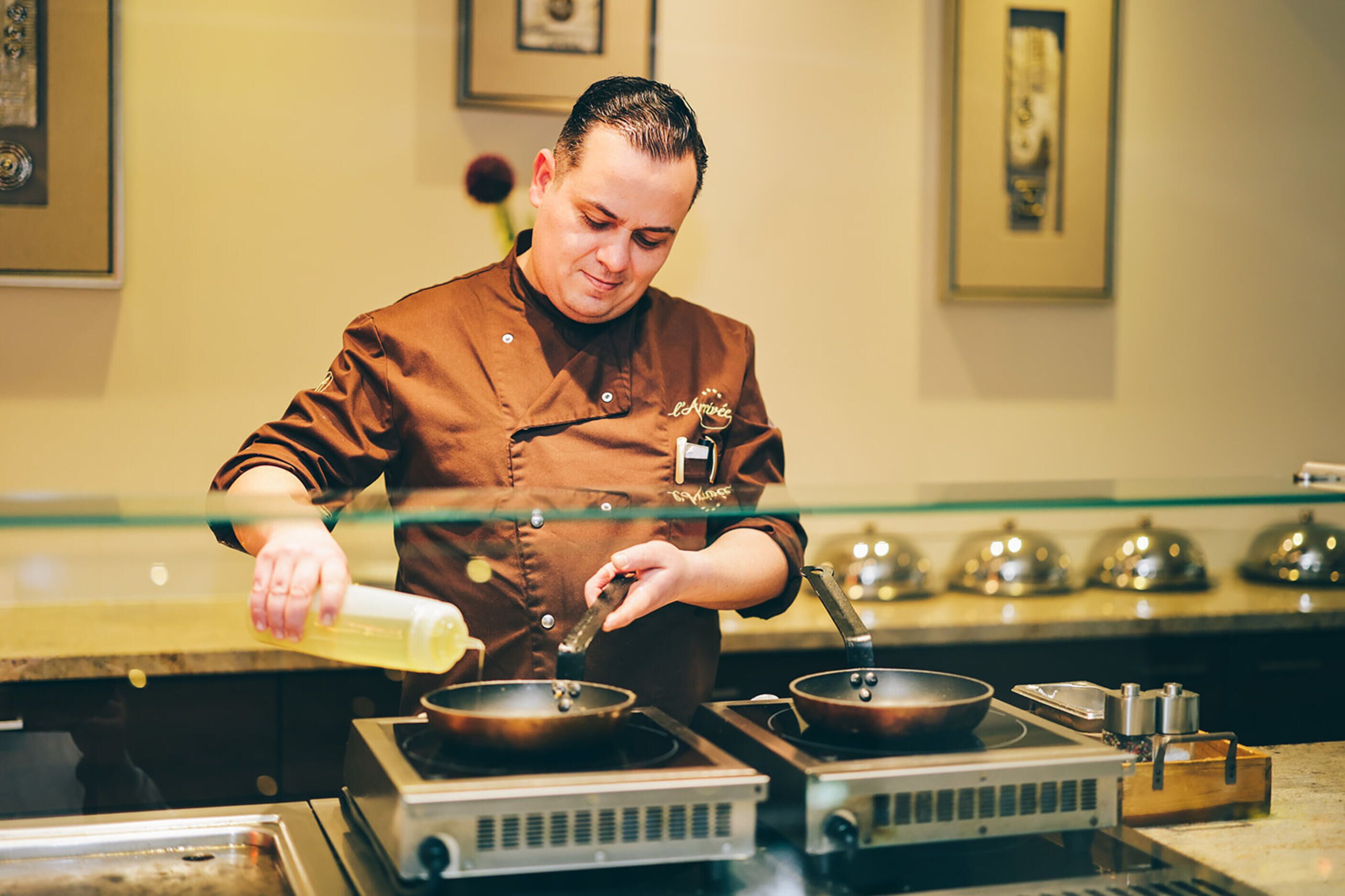 A chef in a kitchen with a stove, pots, and a glass barrier.