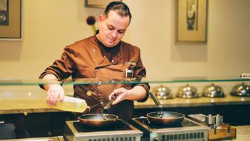 A chef in a kitchen with a stove, pots, and a glass barrier.