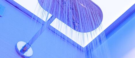 A showerhead with water flowing down a blue wall.