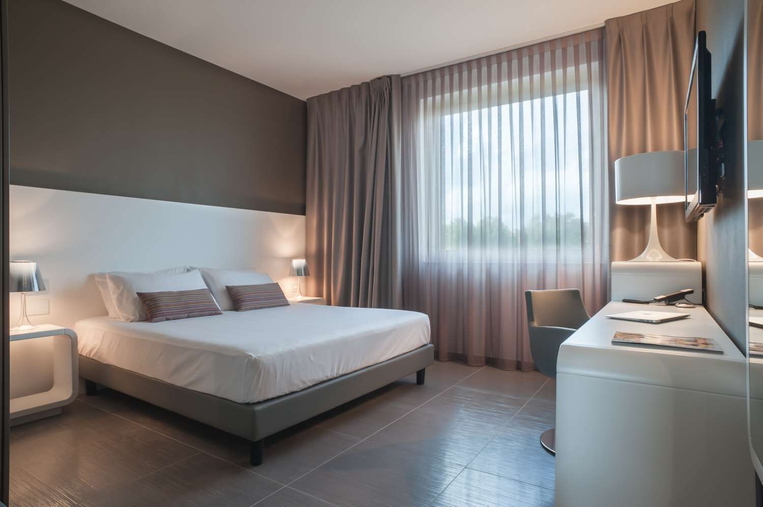 A modern hotel room with a large bed, bedside tables, a desk, and a TV.