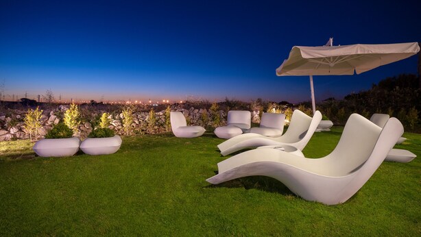 Outdoor lounge chairs and a canopy on a grassy area with a view of the cityscape at dusk. - 8Piuhotel (Lecce)