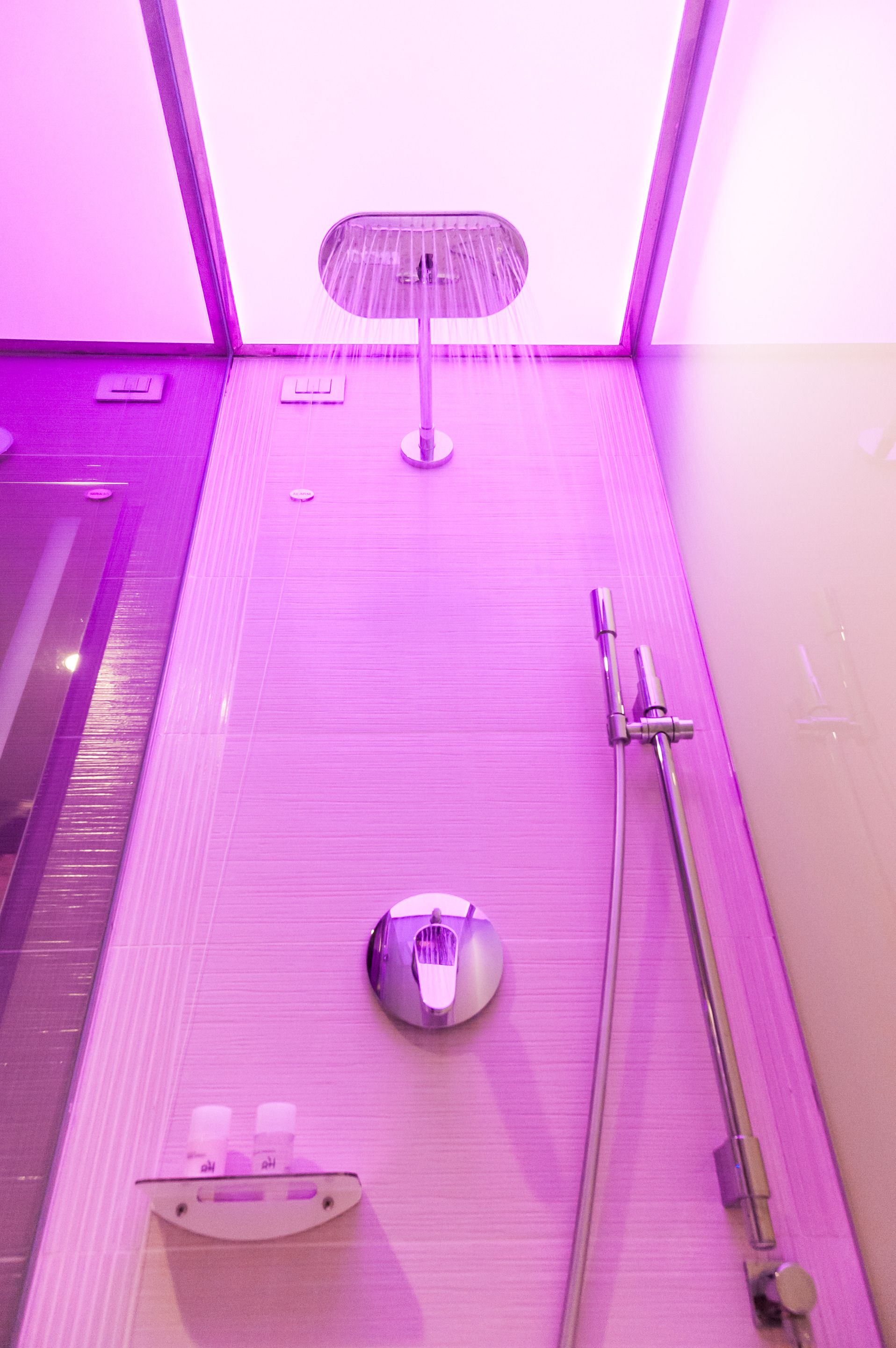 Un baño moderno con ducha, cabezal de ducha manual y un inodoro con mampara de vidrio.
