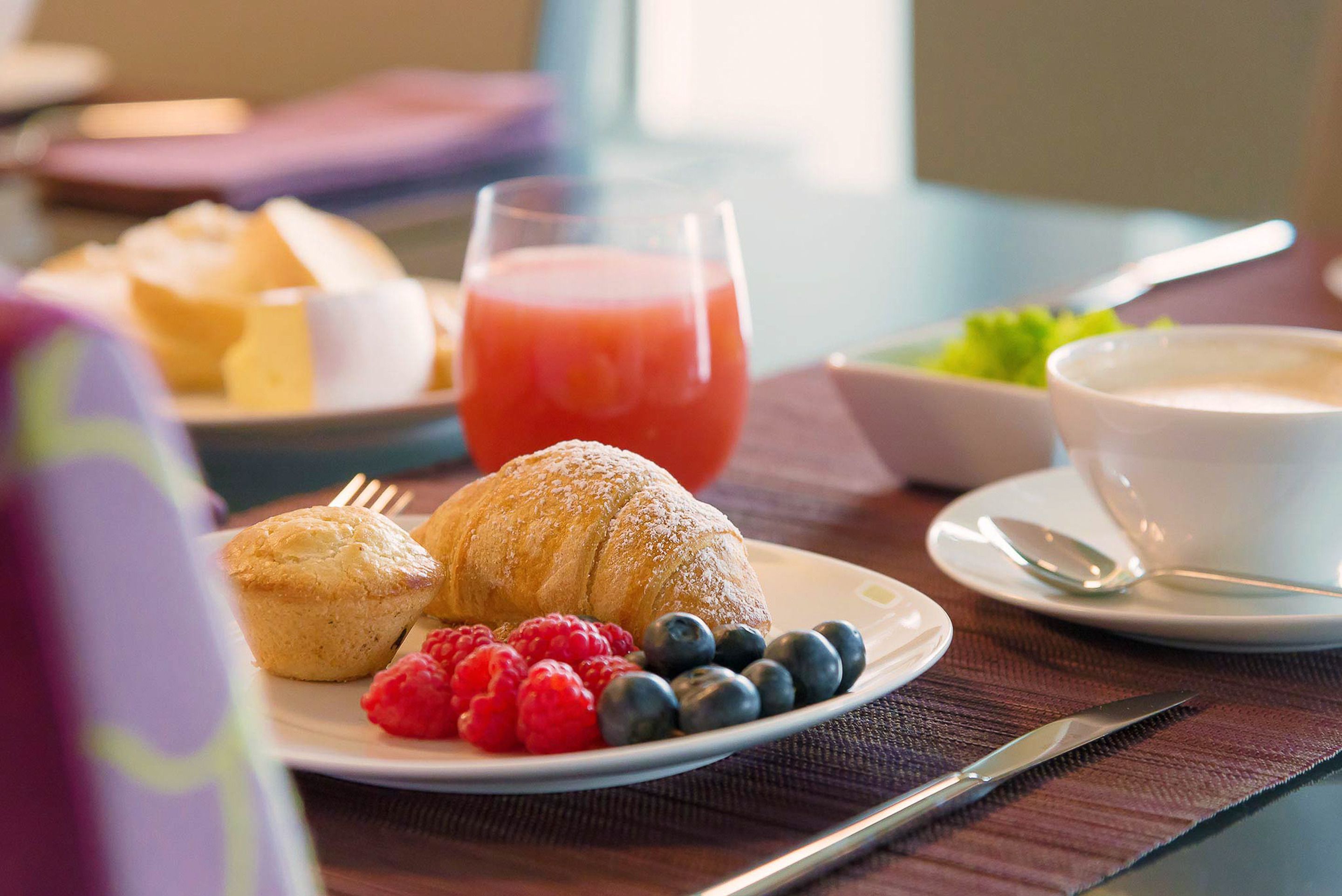 Un desayuno con muffins, frambuesas, arándanos y un vaso de jugo en un plato.