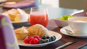 Un desayuno con muffins, frambuesas, arándanos y un vaso de jugo en un plato.