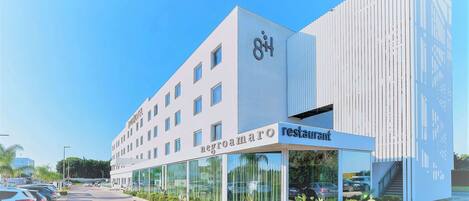 A modern hotel with a restaurant on the ground floor, featuring a clear sky and parked cars.