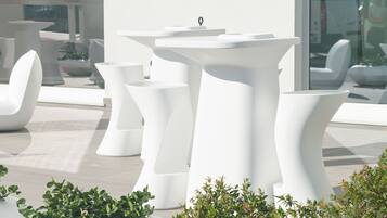 Outdoor seating areas with modern, white, sculptural tables and chairs, surrounded by greenery.