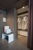 A modern bathroom with a shower area, a bench, and two white robes hanging on a wall.