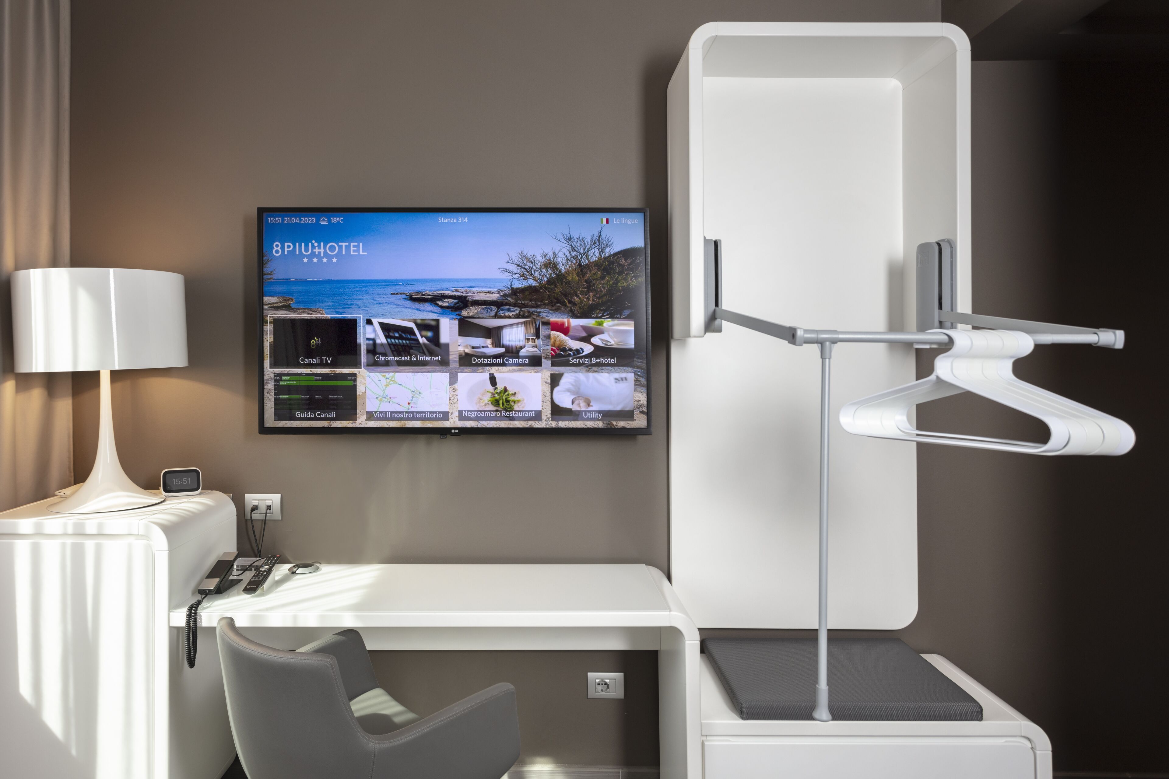 Habitación de hotel moderna con un televisor de pantalla plana mostrando los servicios, un escritorio con lámpara y una silla.