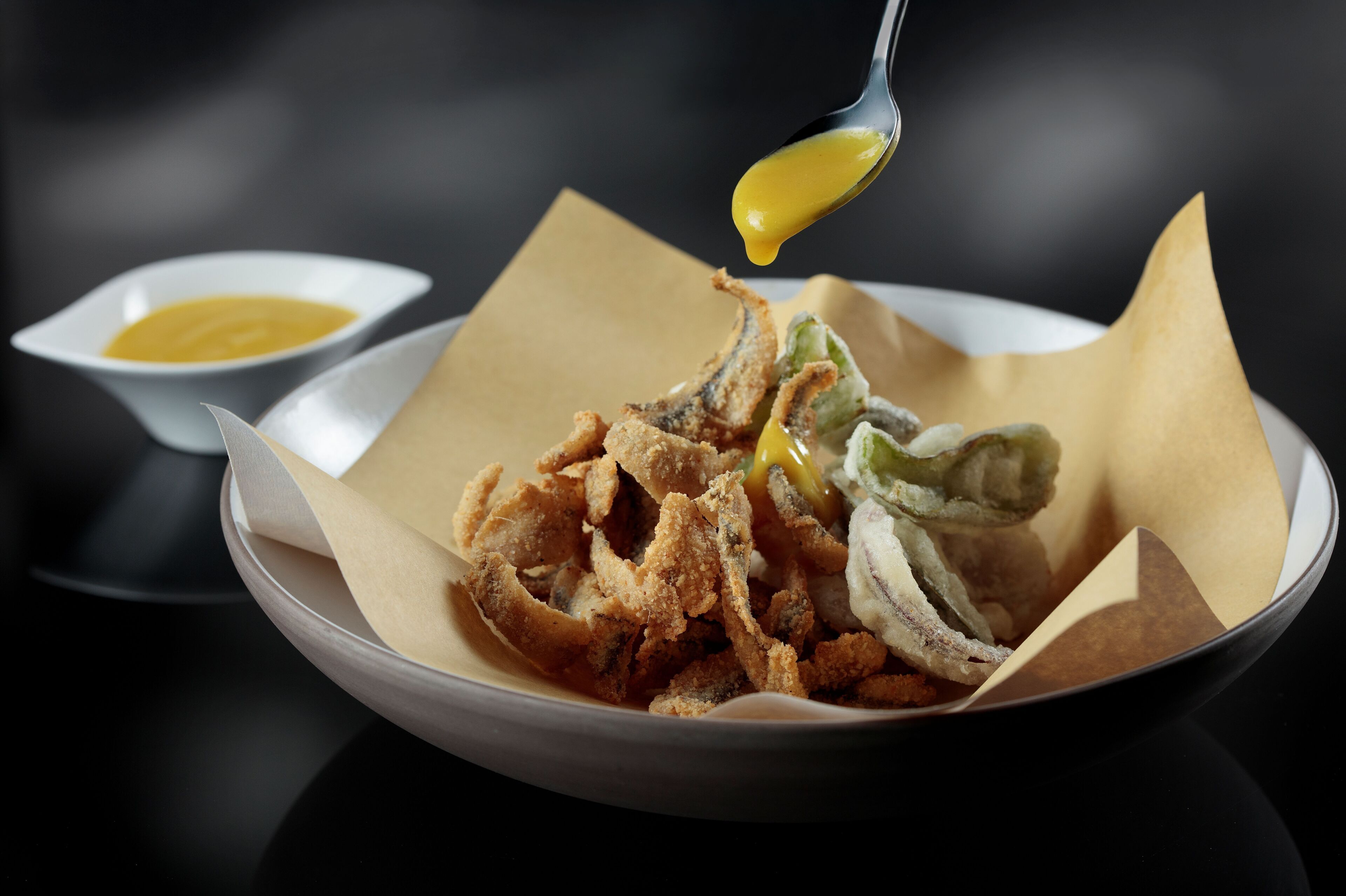 A bowl of fried fish with a dipping sauce and a small bowl of sauce.