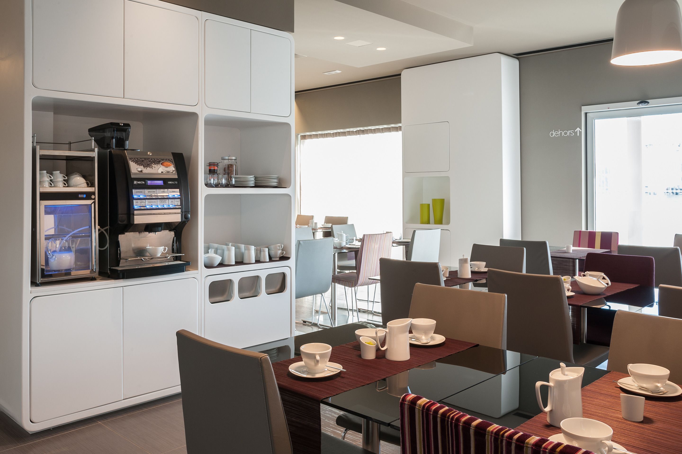 A modern dining area with a coffee machine, multiple tables, and chairs.