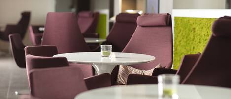 A modern dining area with purple upholstered chairs and white tables, featuring a glass of water on one table.