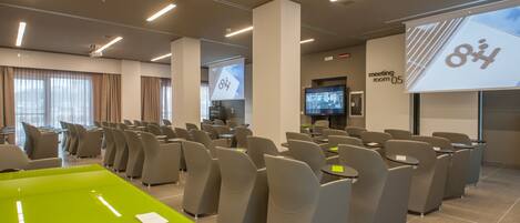 A modern conference room with rows of chairs, a large screen, and a projector.