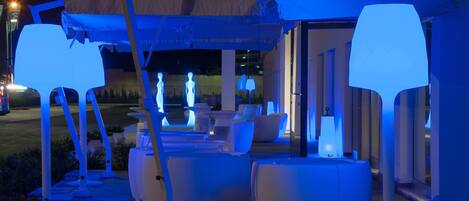 An outdoor seating area with modern white furniture and illuminated blue lights.
