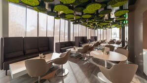 A modern interior with a long seating area, round tables, and green ceiling accents. - 8Piuhotel (Lecce)