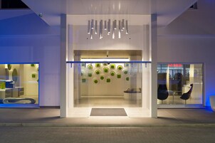 A modern hotel entrance with a glass facade, a reception desk, and a seating area with chairs.