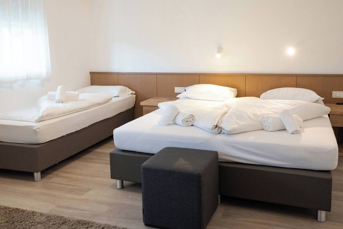 A hotel room with two beds, a small table, and a bench.