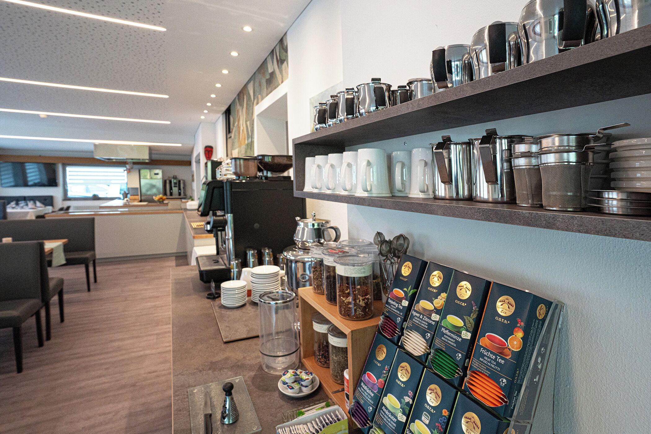 A modern cafe interior with seating, a counter, and shelves with kitchenware.