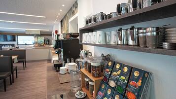 A modern cafe interior with seating, a counter, and shelves with kitchenware.