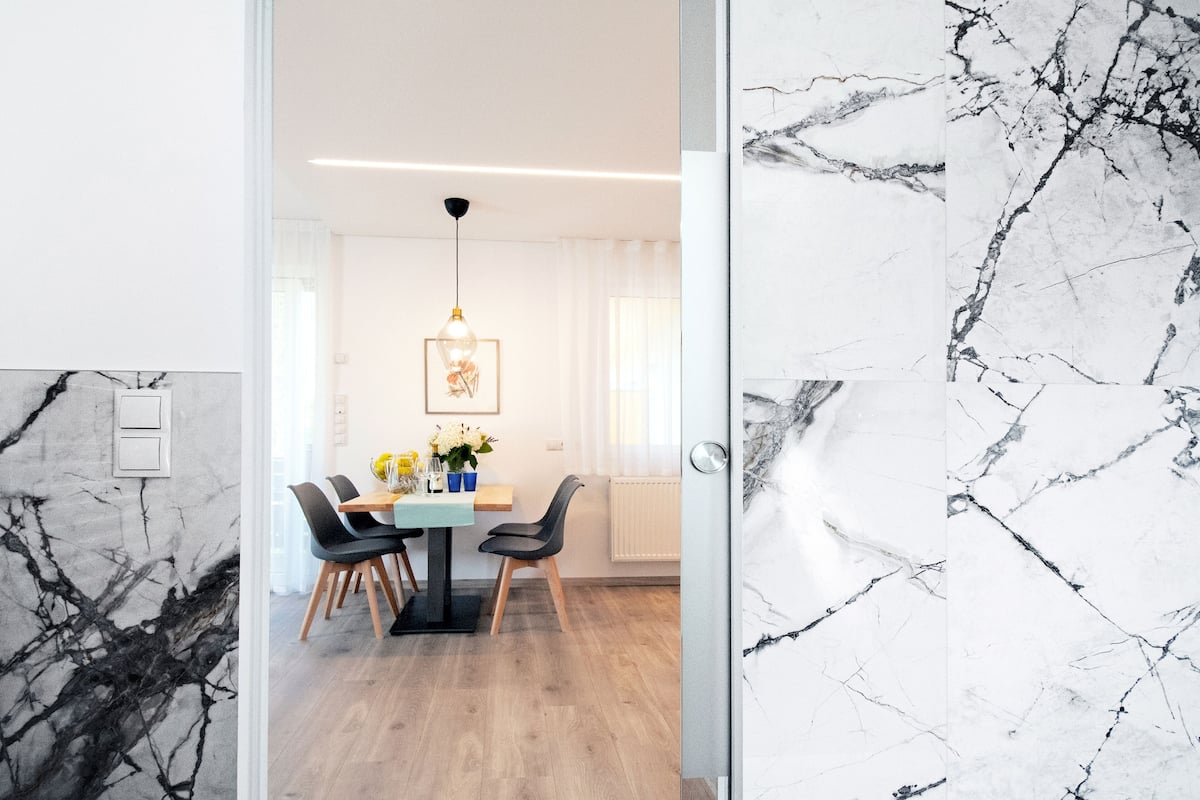A modern dining area with a marble wall, a wooden table, and black chairs.