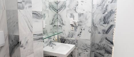 Un baño con lavamanos blanco, cabina de ducha con mampara de vidrio y baldosas con diseño de mármol.