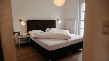 Un dormitorio con cama, mesitas de noche, lámpara de pared y ventana.