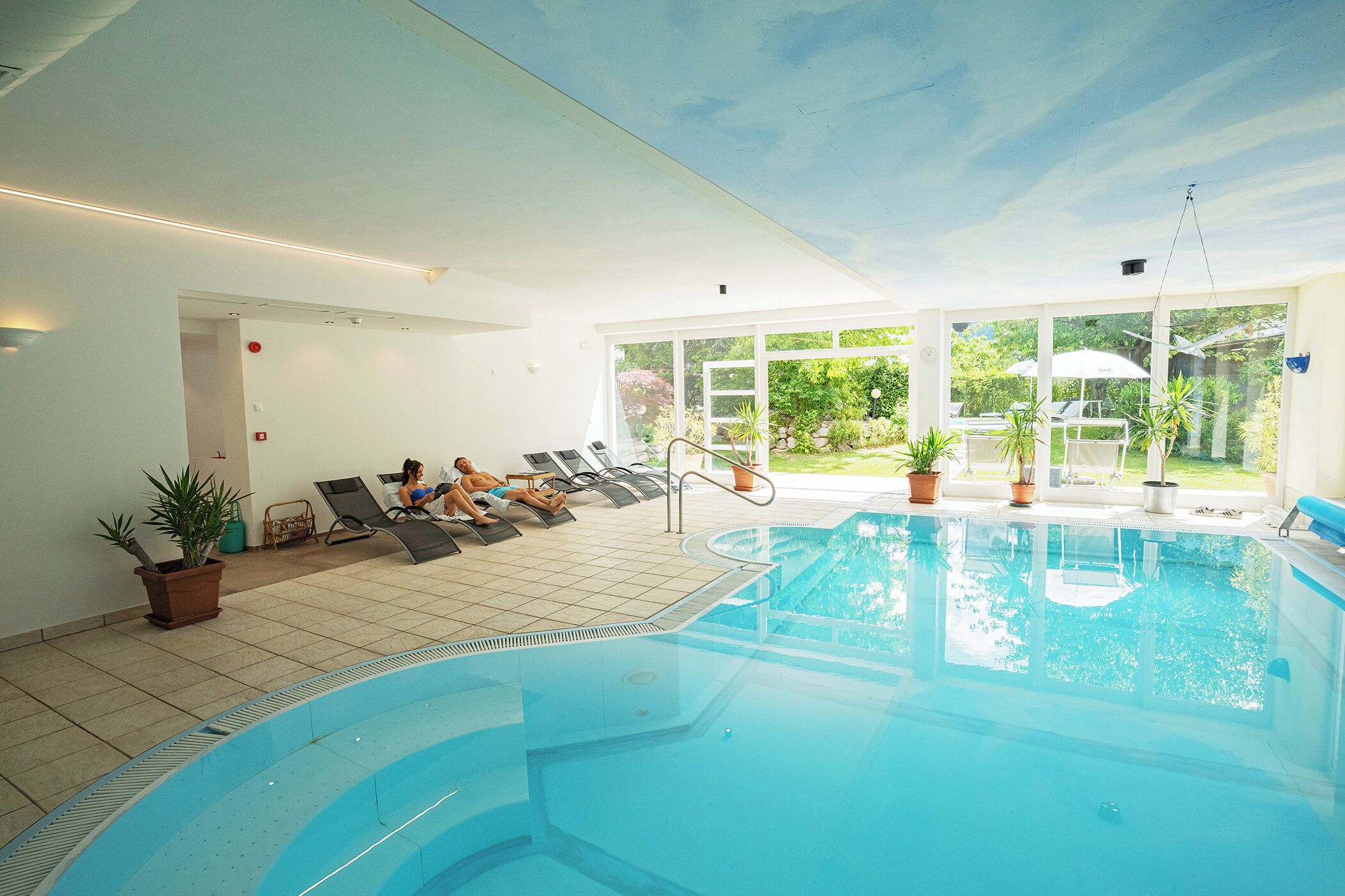 An indoor swimming pool with lounge chairs and potted plants.