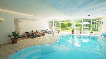An indoor swimming pool with lounge chairs and potted plants.