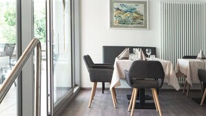 A modern dining area with a glass wall, wooden ceiling, and a painting on the wall. - Parkhotel zur Linde (Silandro)