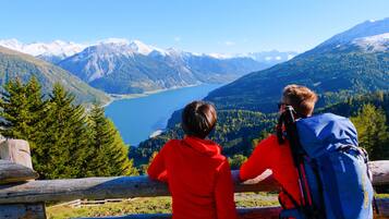 Dos personas con chaquetas rojas de pie junto a una valla de madera, con vistas a un lago y montañas.