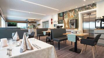 Un'area pranzo moderna con tavoli apparecchiati per due persone, caratterizzata da sedie di design e colori neutri.