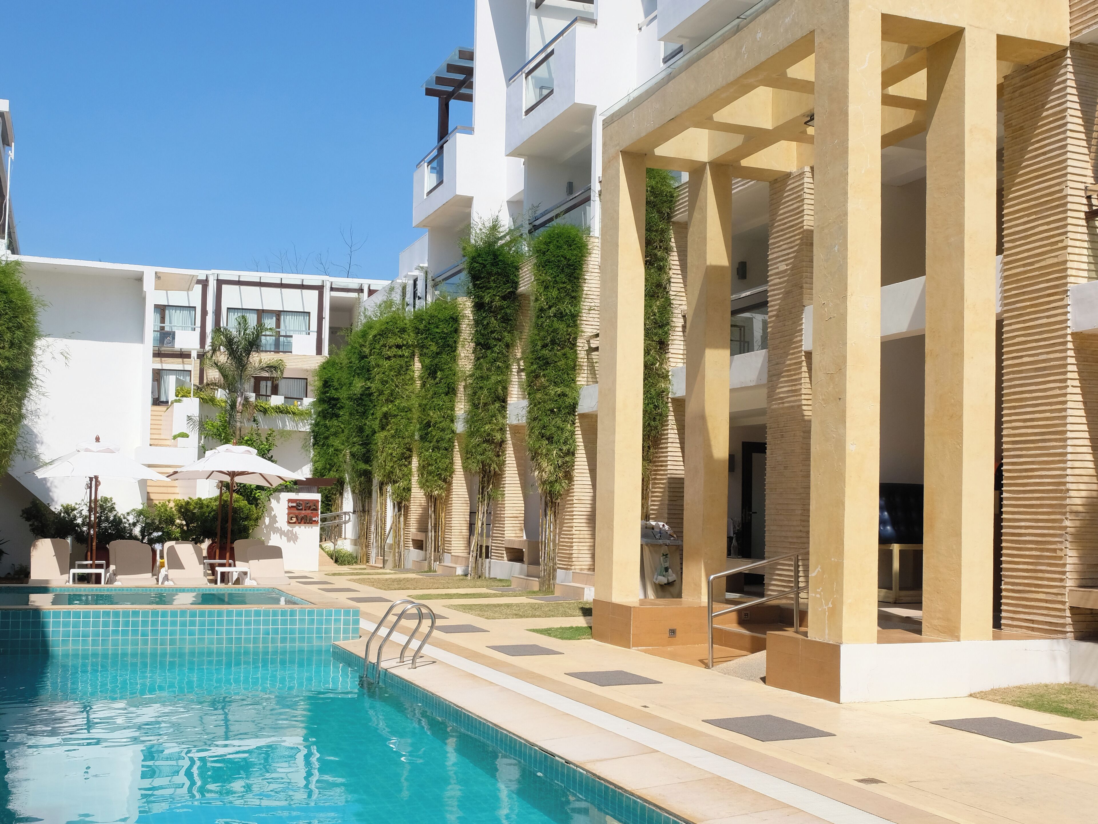 A swimming pool area with a clear blue pool, a sun umbrella, and a lounge chair.
