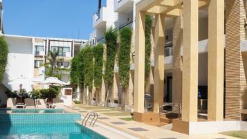A swimming pool area with a clear blue pool, a sun umbrella, and a lounge chair.