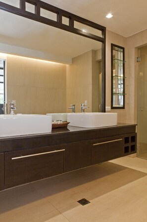 Een moderne badkamer met twee grote witte wastafels, donkere houten kastjes en een grote spiegel.