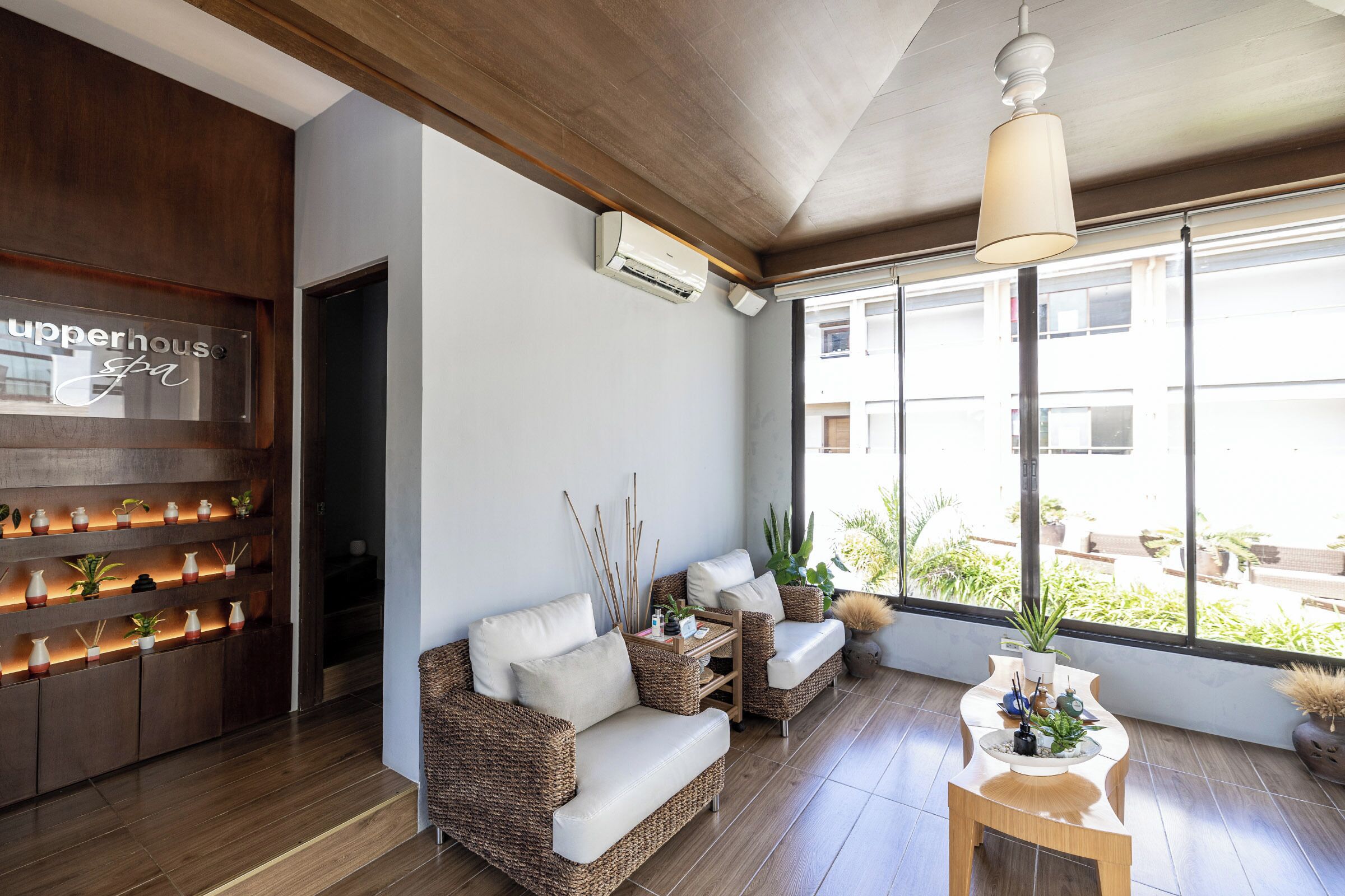 Un interior moderno con sofá, mobiliario de mimbre y un ventanal con vistas a edificios.