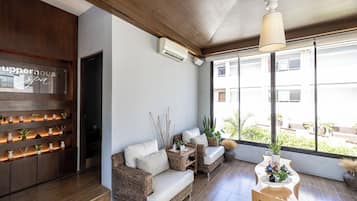 Un interior moderno con sofá, mobiliario de mimbre y un ventanal con vistas a edificios.