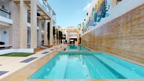 Una piscina con borde de azulejos, rodeada por un edificio de diseño moderno, que incluye una pared de madera y un mural.