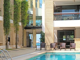 A pool area with lounge chairs and a view of a building with a balcony.
