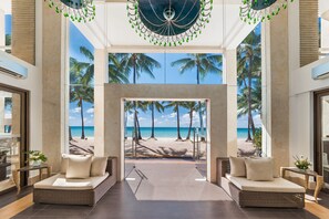 A modern lobby with a large glass wall offering a view of a beach and palm trees. - The District Boracay (Boracay Island)