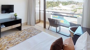 Une chambre d’hôtel équipée d’un lit, d’une télévision, d’un bureau et d’un balcon avec vue sur un complexe hôtelier.