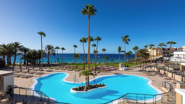 Zwembad van een resort met palmbomen en uitzicht op de oceaan.