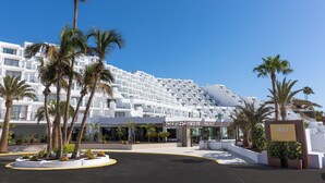 Een modern hotel met een witte gevel, palmbomen en een bord waarop 'RIU' staat.