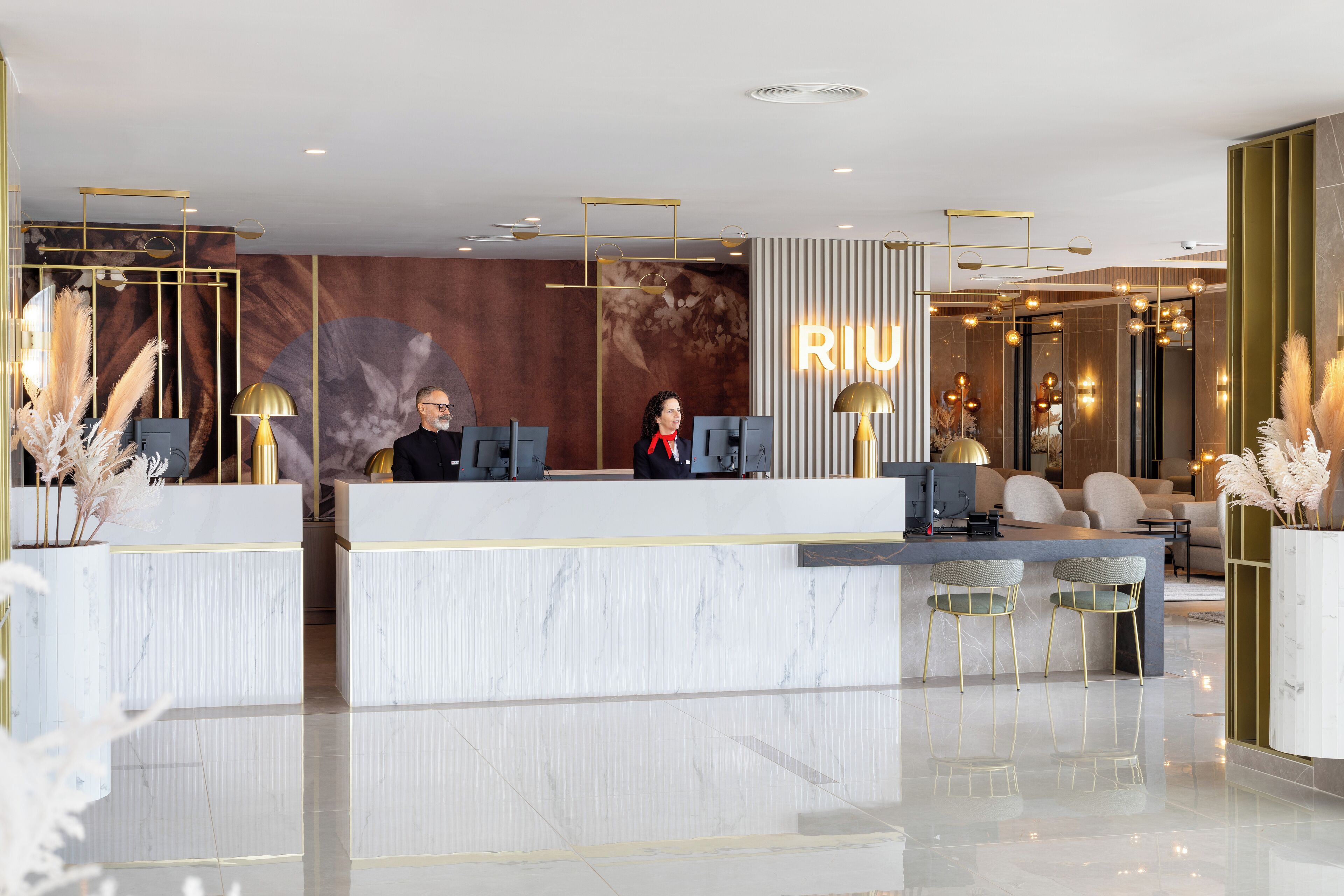 A modern reception area with marble counters, gold accents, and a large 'RIU' sign.