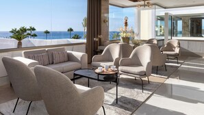 Een moderne woonkamer met een groot raam met uitzicht op de oceaan, ingericht met banken en fauteuils, en een salontafel.