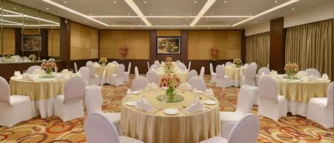 A banquet hall with round tables, white chairs, and floral centerpieces.
