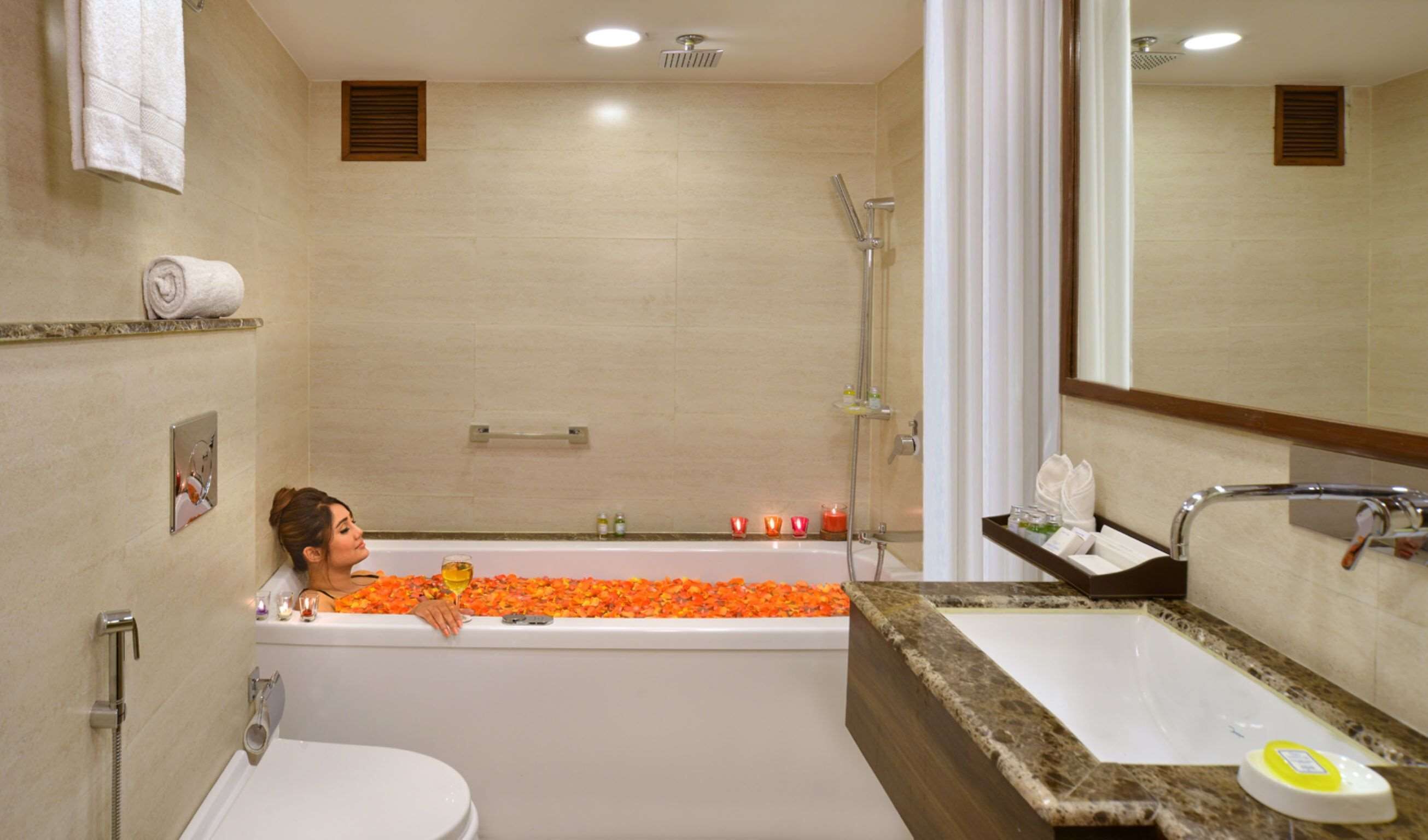 A bathroom with a bathtub filled with orange flowers, a shower, a sink, and a toilet.