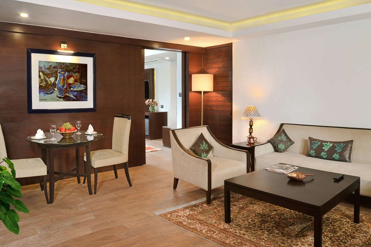 A modern living room with a sofa, two armchairs, a coffee table, and a dining table with a fruit bowl and glasses.