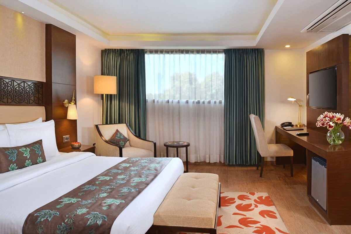 A hotel room with a large bed, two chairs, a desk with a TV, and a small table.