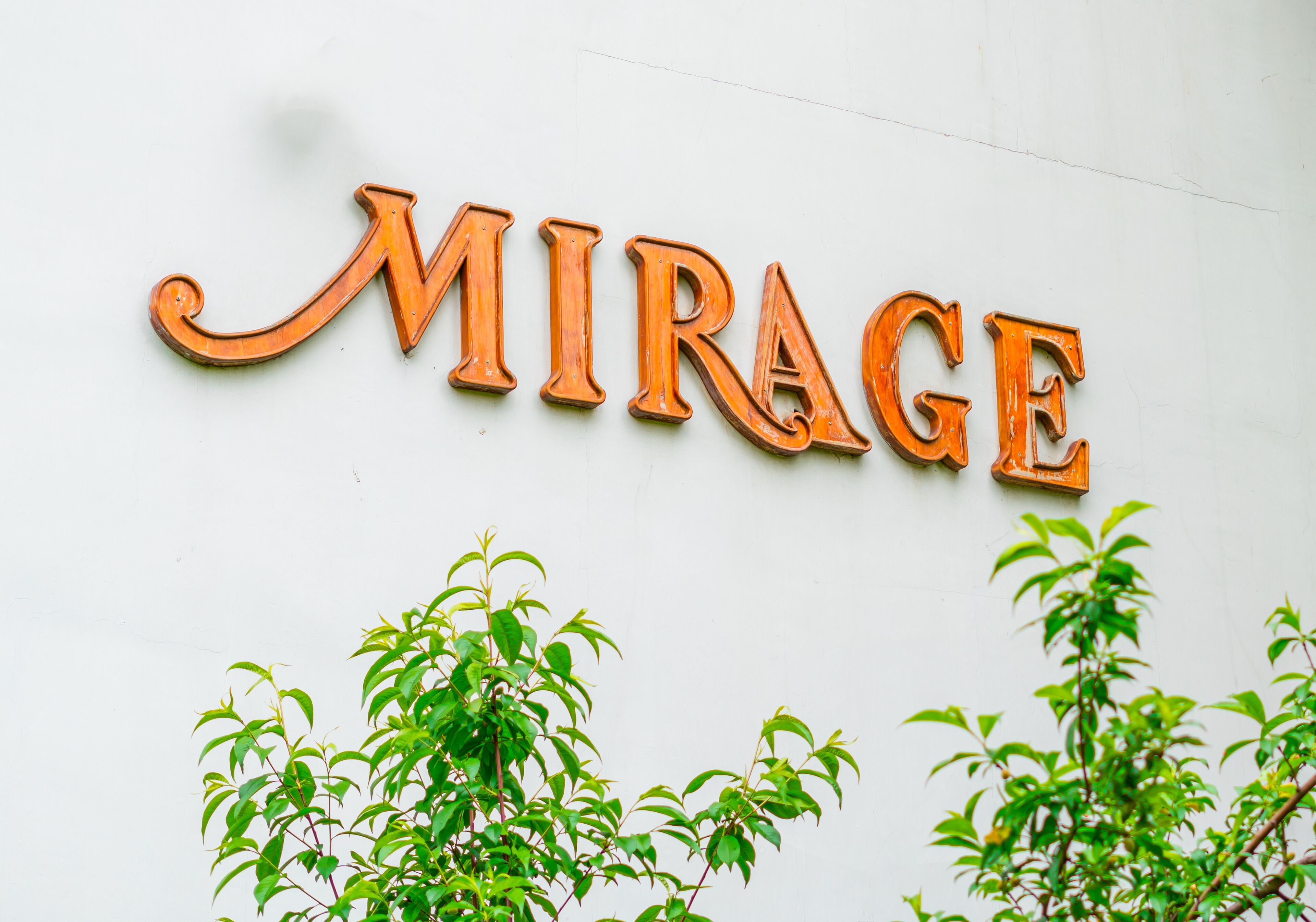 A sign with the word "MIRAGE" in large, wooden letters mounted on a white wall.