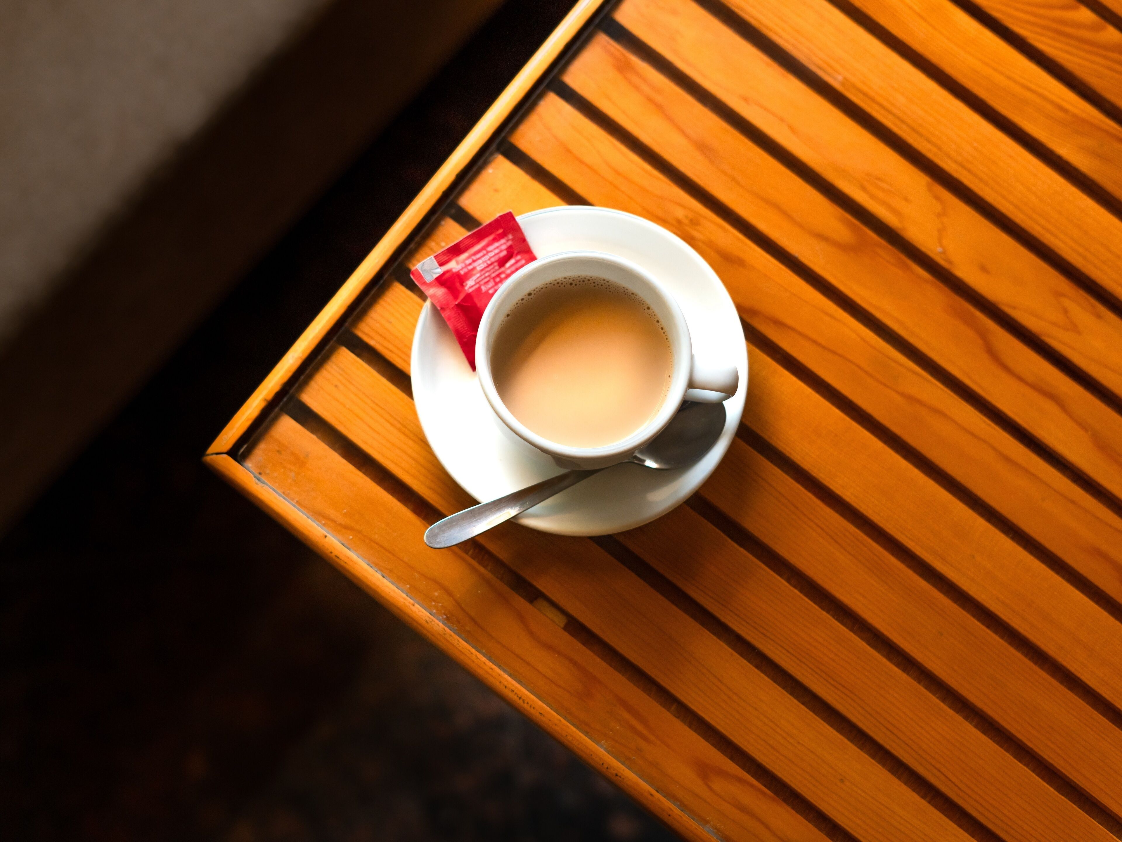 A cup of coffee on a wooden table with a spoon.
